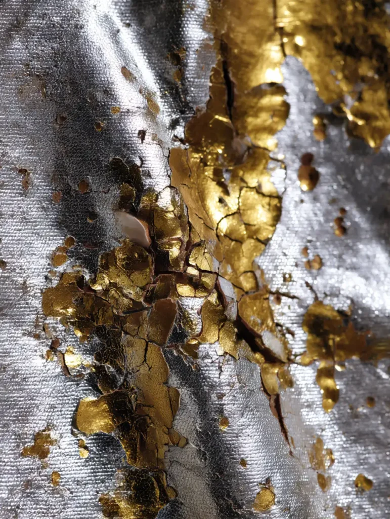 Close-up of metallic fabric showing cracks and peeling texture


